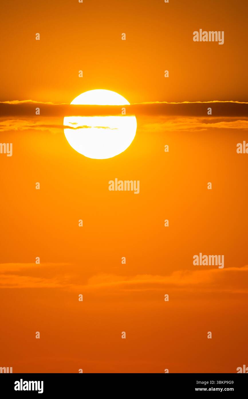 Il sole dorato si illumina attraverso sottili nuvole nel vivace cielo arancione all'alba o al tramonto, creando un'atmosfera calda e da sogno Foto Stock