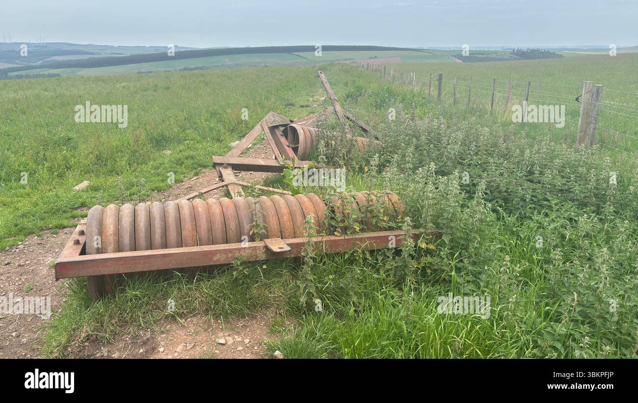 Rusty abbandonò i rulli agricoli che riposavano nell'erba sovrastata, mostrando metallo intempestivo e decadimento rurale nella campagna scozzese. Foto Stock