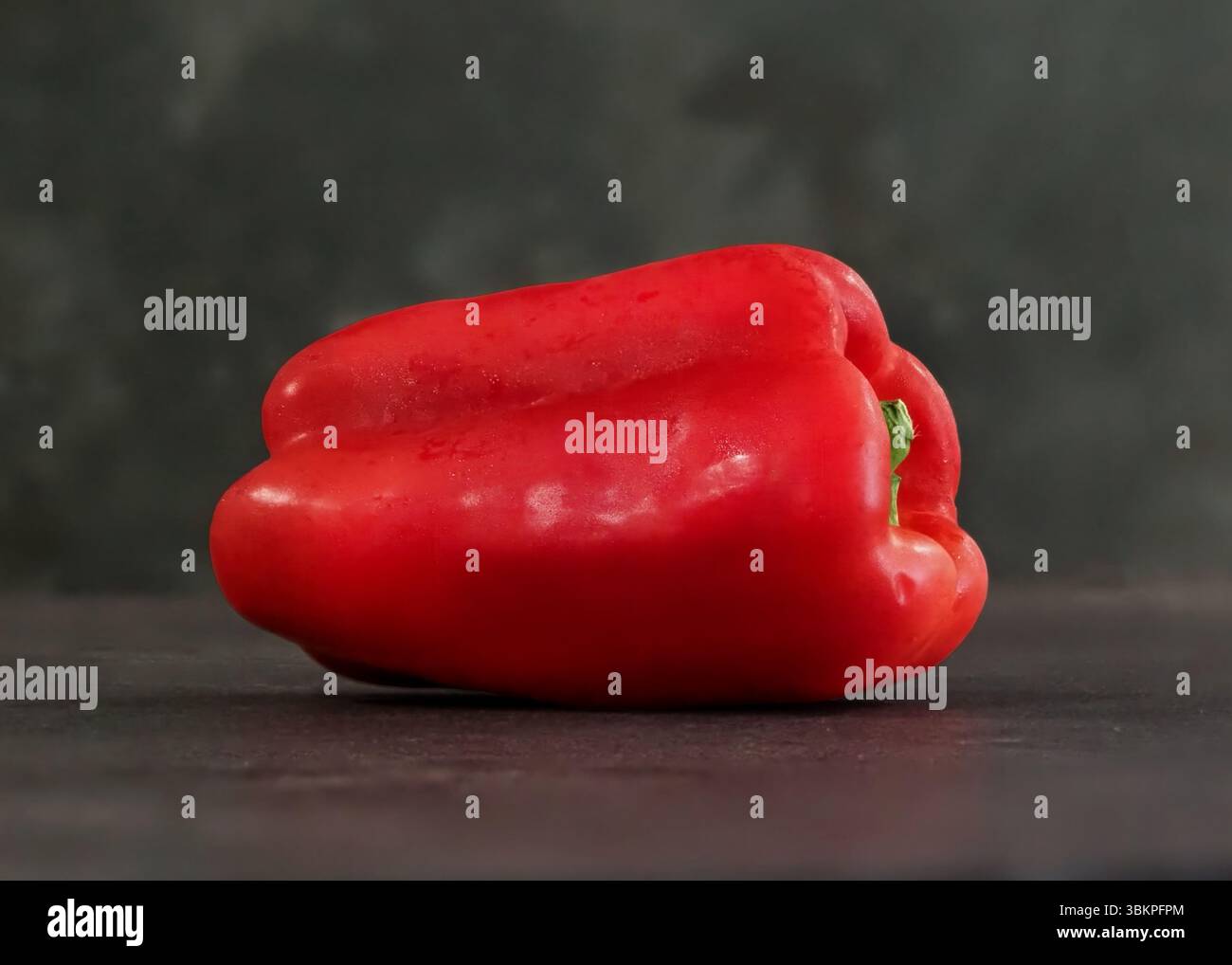 Un peperone rosso si siede su un bancone. E' tagliato a metà. Lo stelo è verde. Il pepe è fresco Foto Stock