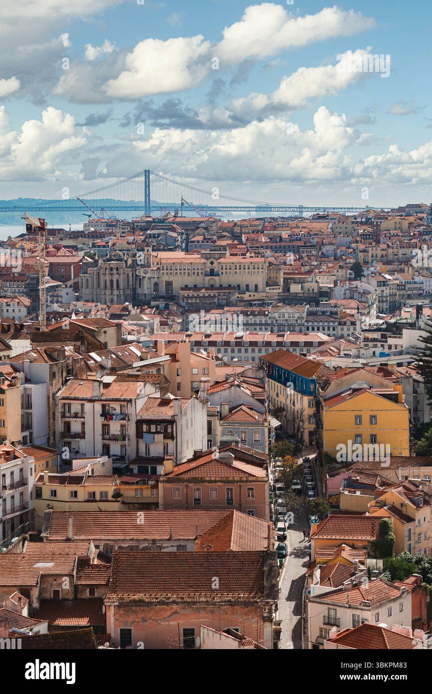 Vibrante paesaggio urbano di Lisbona caratterizzato da tradizionali tetti rossi, architettura storica e il famoso Ponte 25 de Abril sotto un cielo spettacolare, perfetto per viaggi e ispirazione urbana. Foto Stock