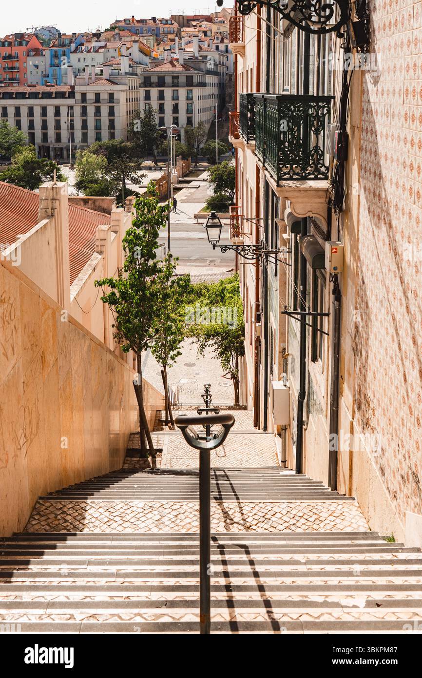 Affascinante scalinata di Lisbona bagnata dalla luce del sole, caratterizzata da edifici piastrellati classici, balconi in ferro e un vivace paesaggio urbano. Perfetto per viaggi, architettura e temi di esplorazione urbana. Foto Stock