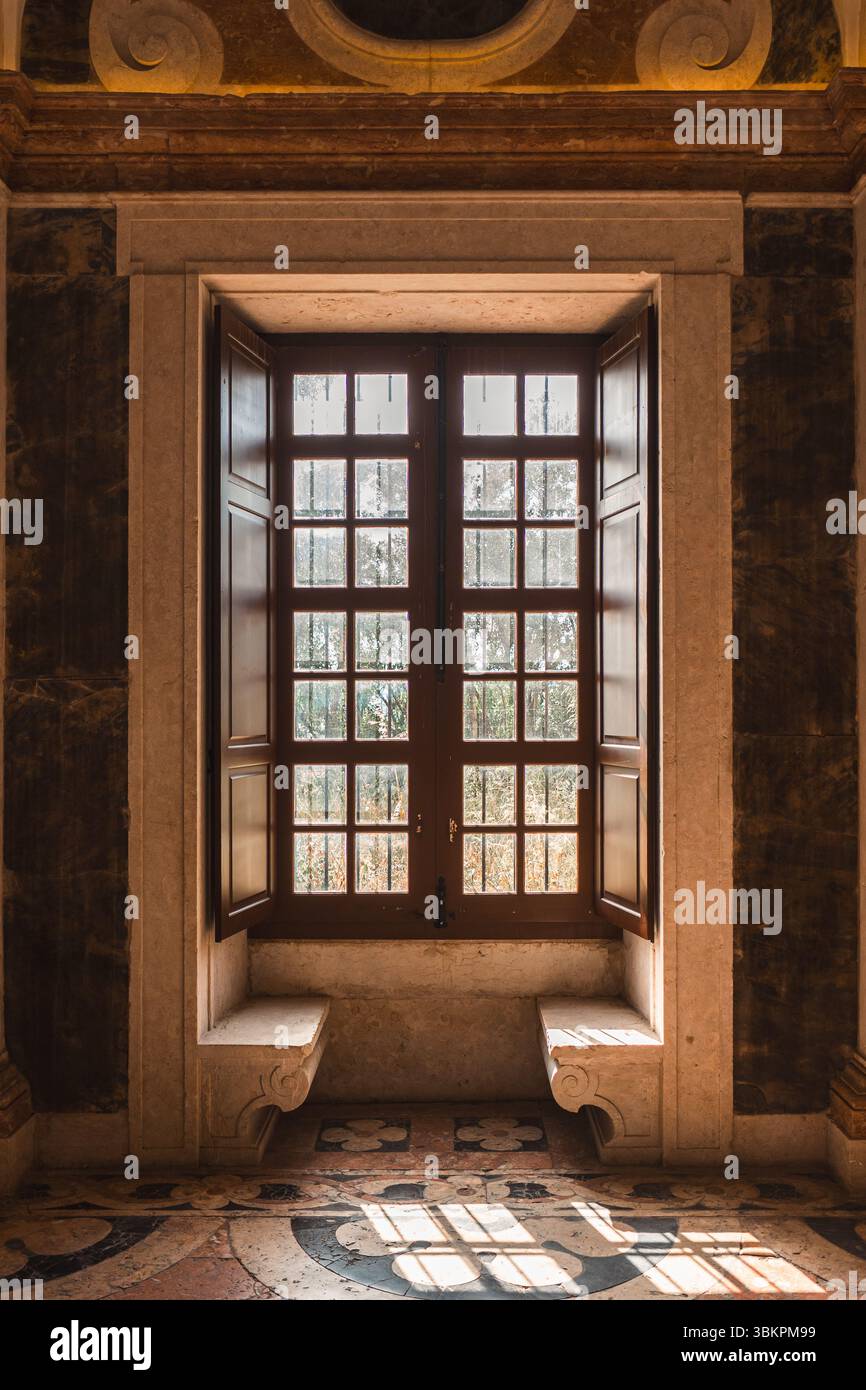 Splendida finestra illuminata dal sole con panche classiche in pietra e dettagli decorati in uno storico palazzo di Lisbona, perfetta per l'architettura, i viaggi e l'ispirazione per il patrimonio culturale. Foto Stock