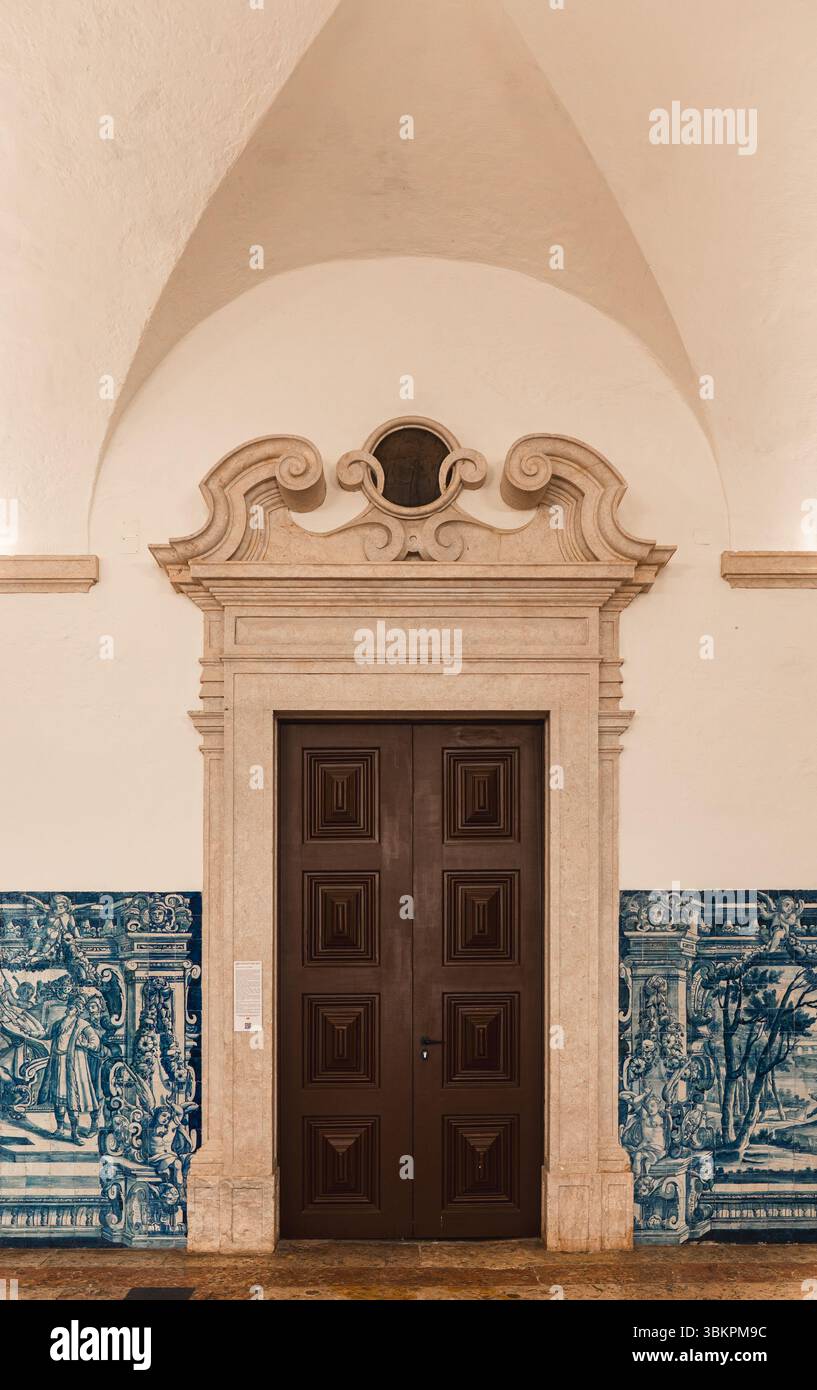 Architettura classica di Lisbona caratterizzata da una grande porta in legno incorniciata da ornati in pietra e tradizionali piastrelle blu azulejo, perfetta per il patrimonio culturale, i viaggi e l'ispirazione per il design. Foto Stock