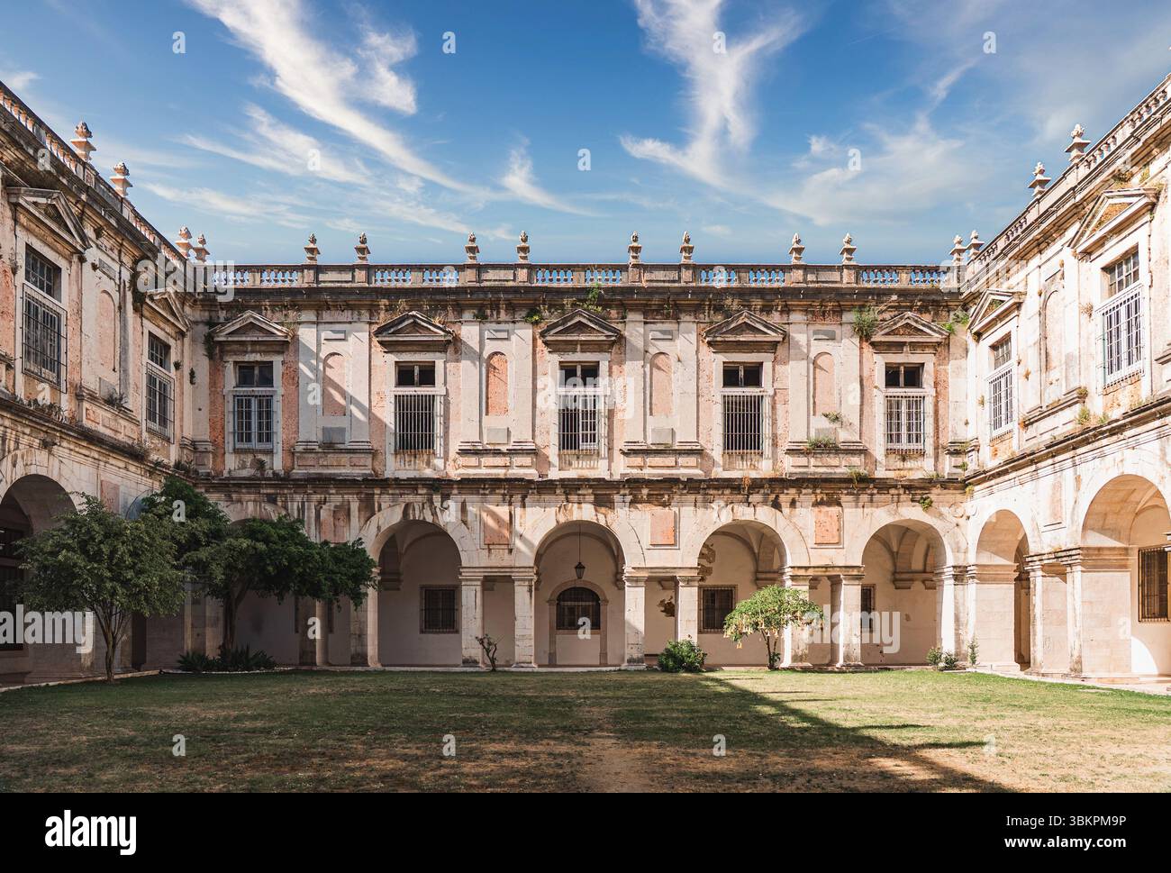 Splendido cortile di un antico monastero di Lisbona, Portogallo, con passaggi ad arco, muri in pietra intemprati e un tranquillo spazio aperto sotto un vivace cielo blu. Foto Stock