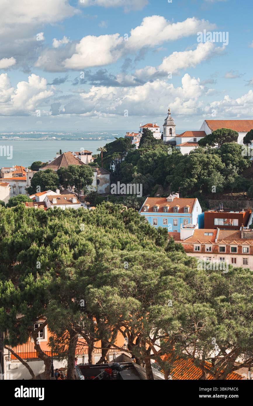 Splendida vista panoramica di Lisbona con vegetazione lussureggiante, tetti vivaci, chiesa storica e il fiume Tago sotto un cielo spettacolare. Perfetto per viaggi, turismo e paesaggi urbani. Foto Stock