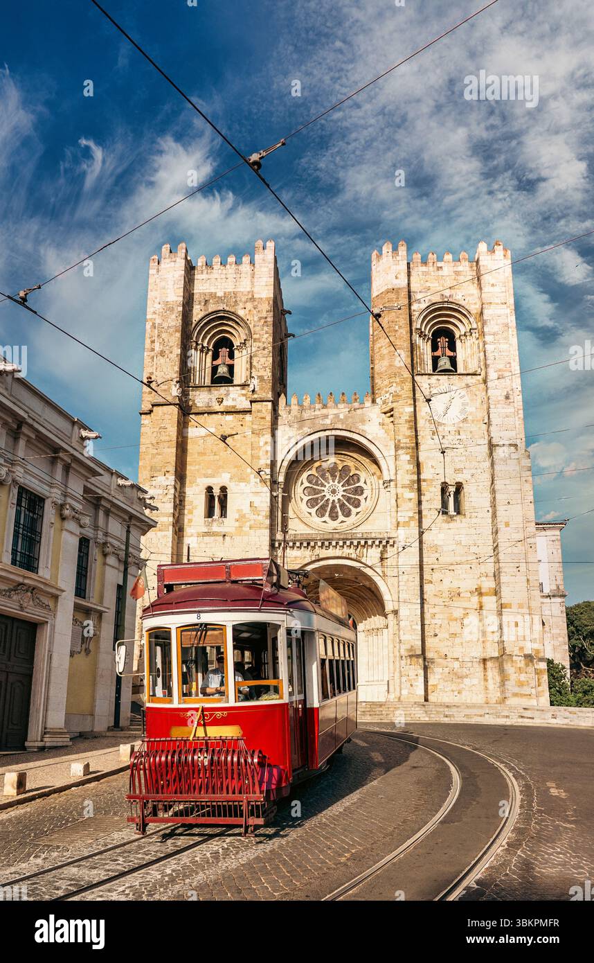 Il tram rosso d'epoca passa davanti all'iconica cattedrale se di Lisbona, Portogallo, catturando il fascino, la storia e l'atmosfera vibrante della città in un soleggiato Foto Stock