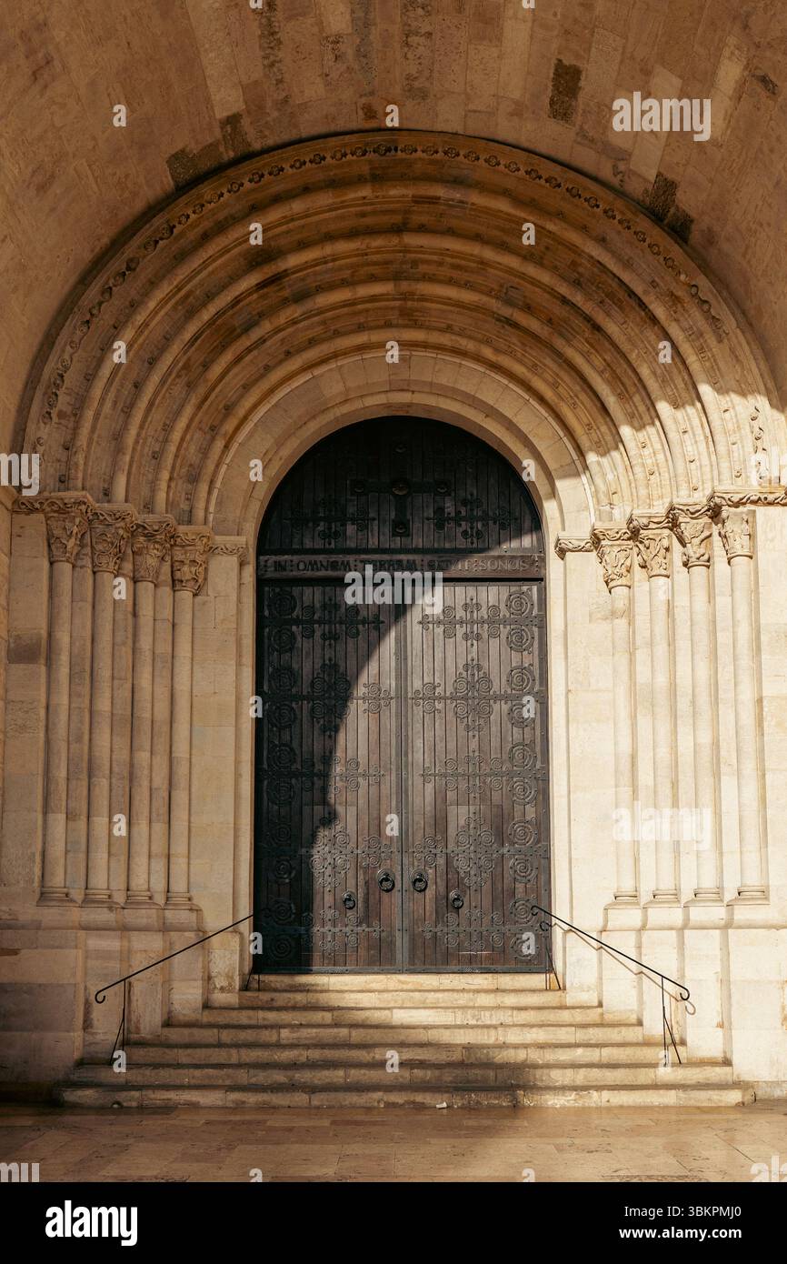 Splendida entrata della chiesa romanica a Lisbona, Portogallo, caratterizzata da intricati archi in pietra e una grande porta in legno, ideale per architettura, viaggi e concetti storici. Foto Stock