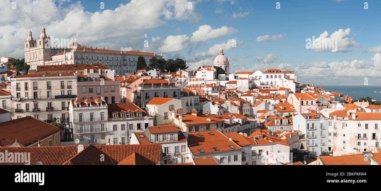 Splendida foto panoramica del quartiere Alfama di Lisbona, con i tradizionali tetti rossi, l'architettura storica e il paesaggio urbano sotto un luminoso blu Foto Stock