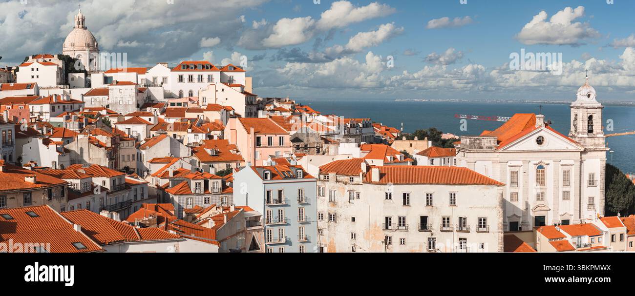 Splendida foto panoramica del quartiere Alfama di Lisbona, caratterizzato da iconici tetti rossi, architettura storica e il fiume Tago sotto un cielo vivace. Per Foto Stock