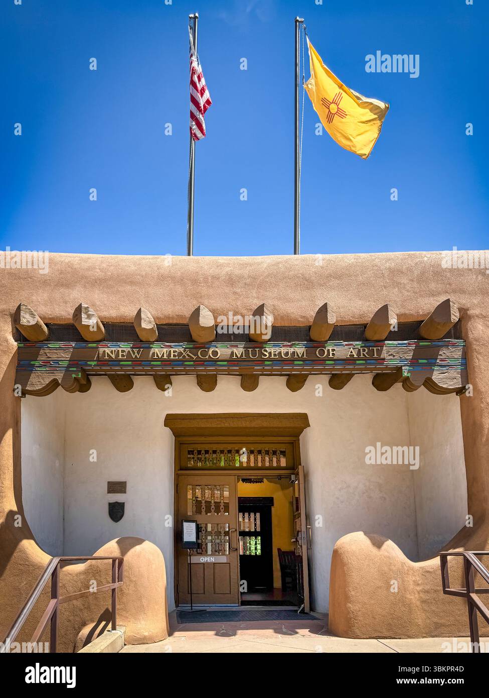Primo piano dell'ingresso al Museo d'arte del New Mexico, con code viga, e in stile Santa Fe e bandiere DEL NEW MEXICO e degli Stati Uniti che sventolano sopra la porta aperta di Santa Fe, NEW MEXICO Foto Stock