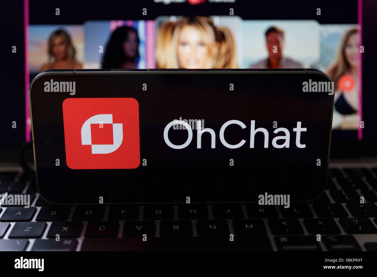 Logo OhChat visualizzato sullo smartphone appoggiato sulla tastiera del computer portatile con ritratti sfocati di donne sullo schermo, che suggeriscono contenuti digitali per adulti. Stafford, ONU Foto Stock