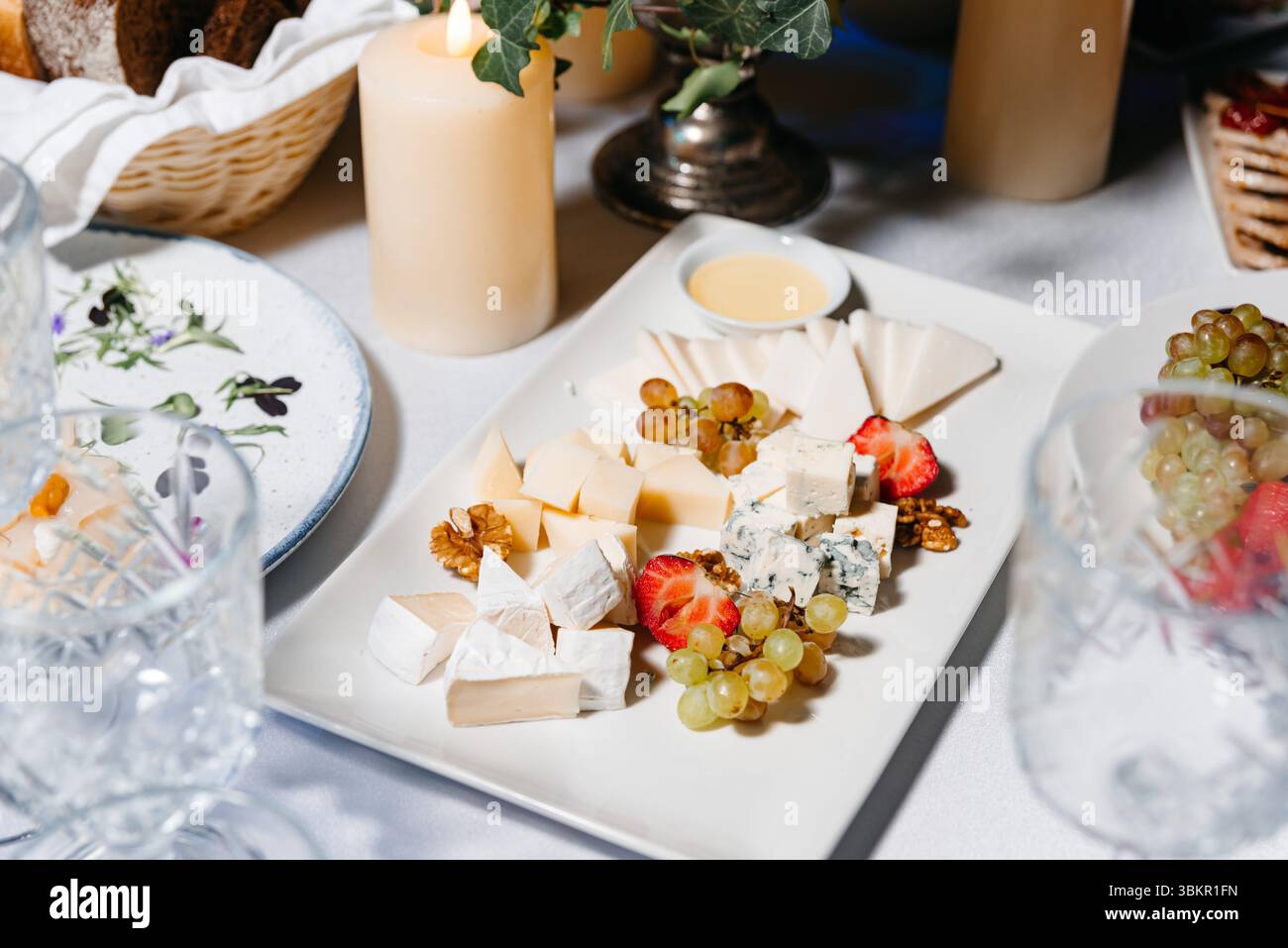 Elegante tagliere di formaggi servito con frutta assortita, noci e salsa subacquea, ideale per eventi di alto livello e riunioni formali. Foto Stock