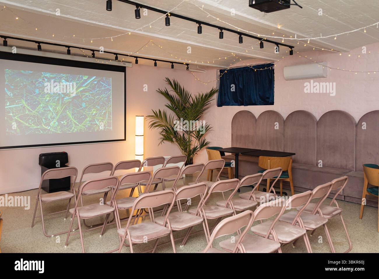 Moderno spazio eventi con schermo proiettore, file di sedie, illuminazione soffusa ed elementi decorativi per presentazioni o riunioni. Foto Stock