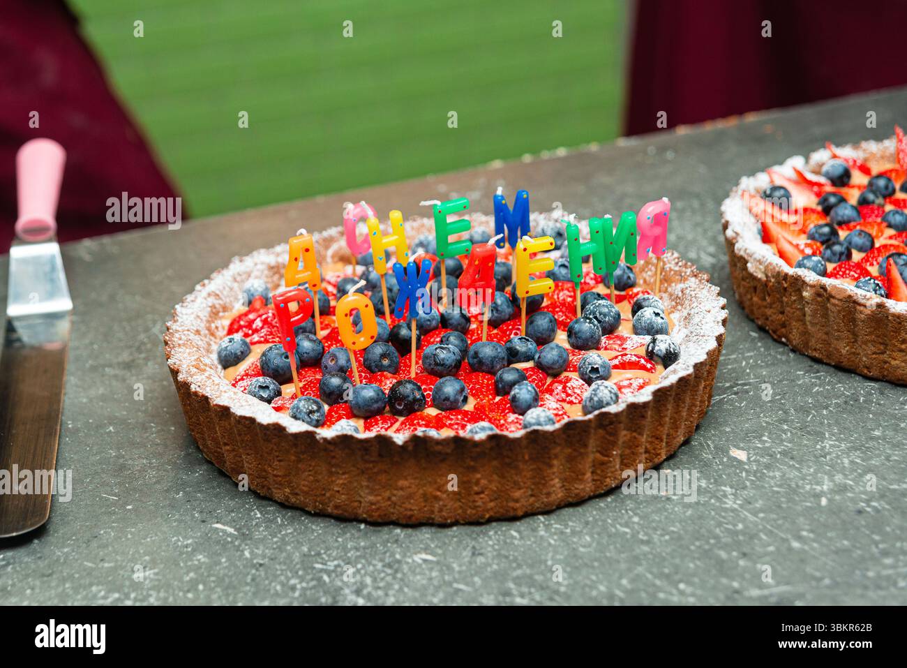 Crostata di frutta natalizia condita con fragole e mirtilli, decorata con candele colorate "Happy Birthday" scritte in russo. Foto Stock