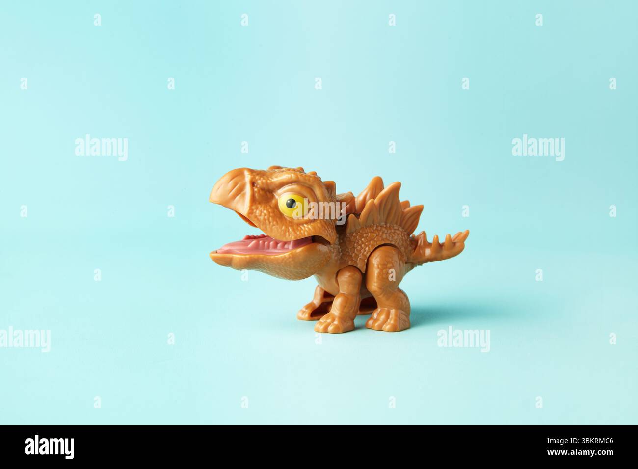 Piccolo e carino giocattolo di stegosauro in plastica in azione su sfondo ciano Foto Stock