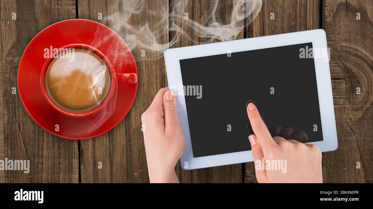 Il tablet bianco dal design piatto poggia in due mani su un piano in legno con una tazza di caffè Foto Stock
