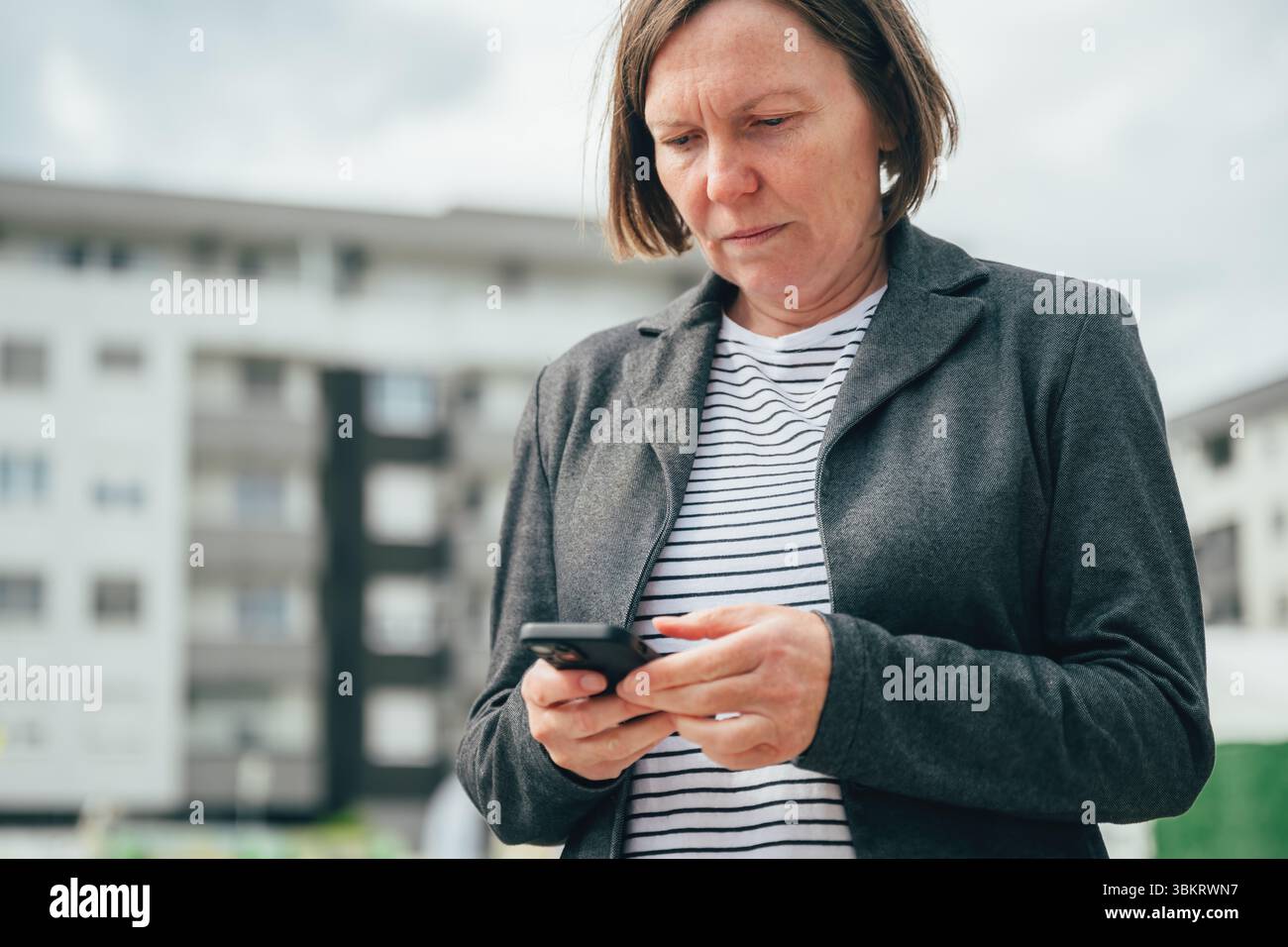 Donna d'affari che digita un messaggio di testo sullo smartphone sulla strada del centro città, attenzione selettiva Foto Stock