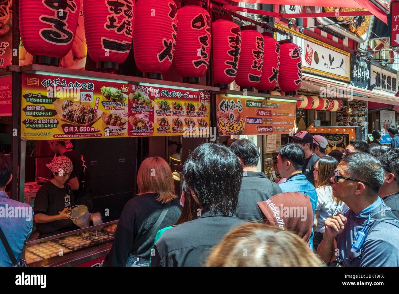 La gente fa la fila al banco da asporto che vende cibo tradizionale giapponese fritto Takoyaki a Dotonbori, una delle principali destinazioni turistiche di Osaka, in Giappone. Foto Stock