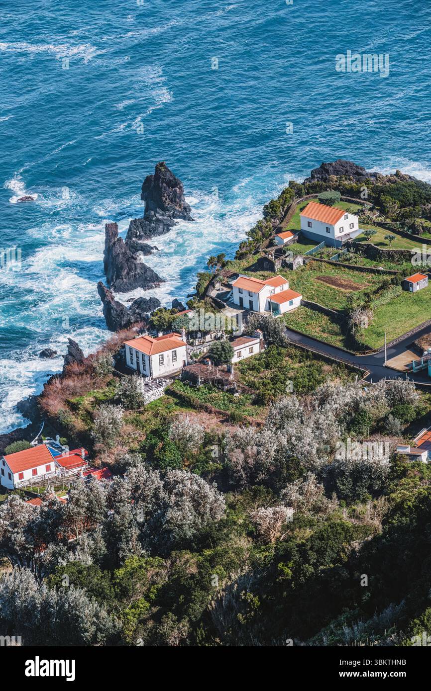 Un pittoresco villaggio costiero è annidato precariamente sulle scogliere dell'isola di Sao Jorge, offrendo splendide vedute del potente Oceano Atlantico. Trave Foto Stock