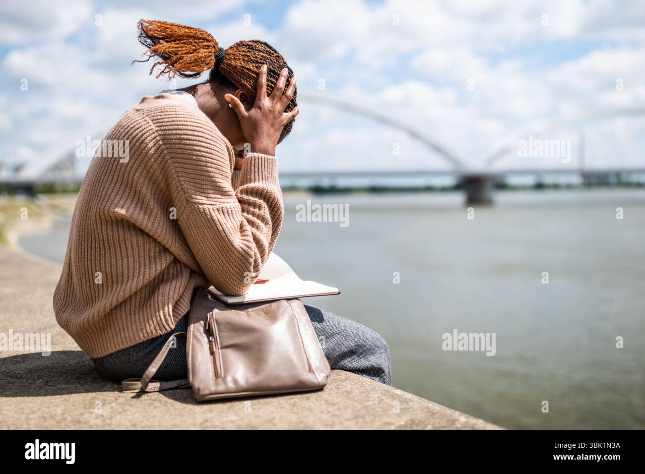 Ritratto di una giovane donna nera scontenta che è seduta vicino al fiume in città. Foto Stock