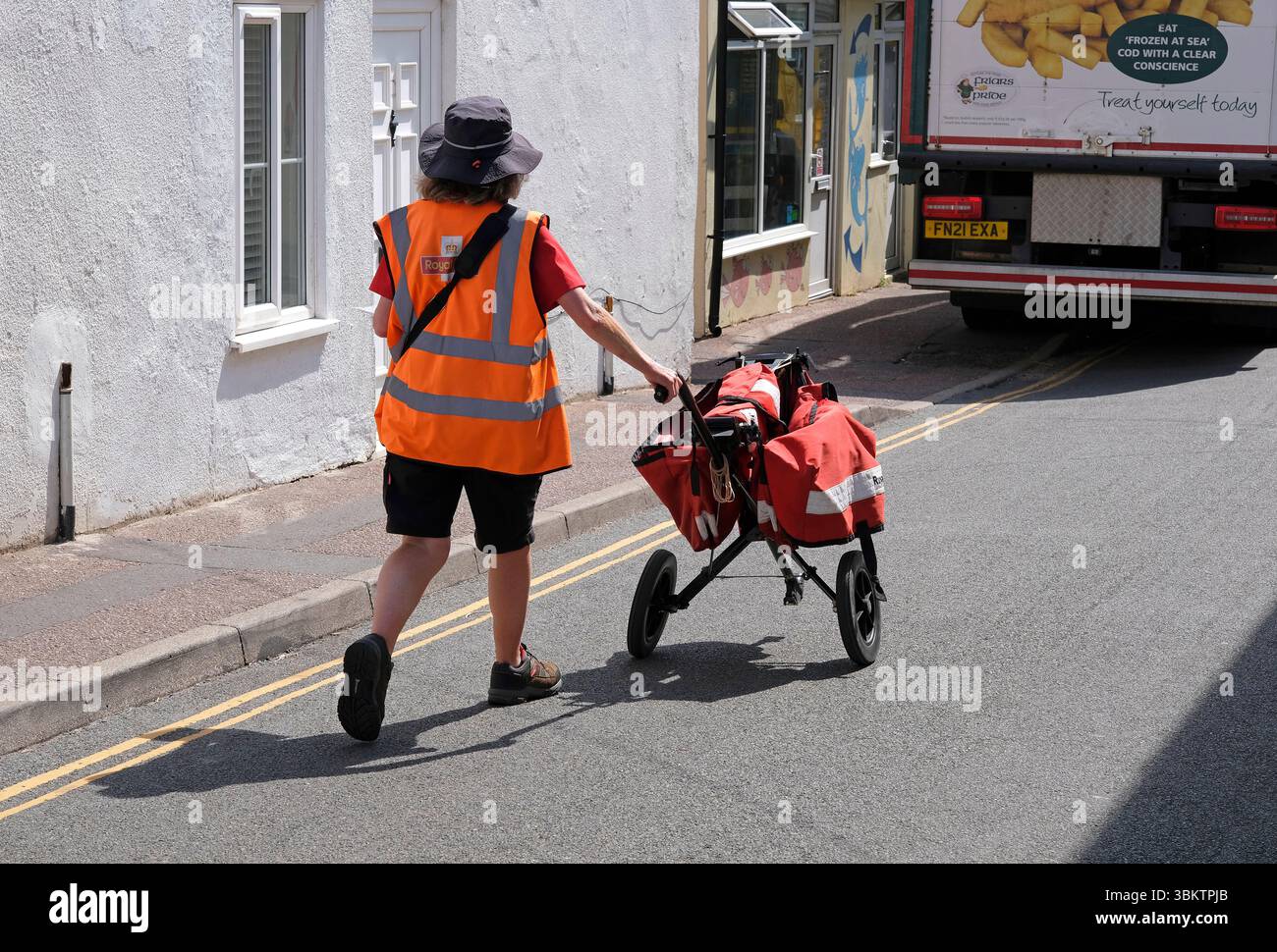 posta donna che spinge il carrello della posta reale lungo la strada, sheringham, nord norfolk, inghilterra Foto Stock