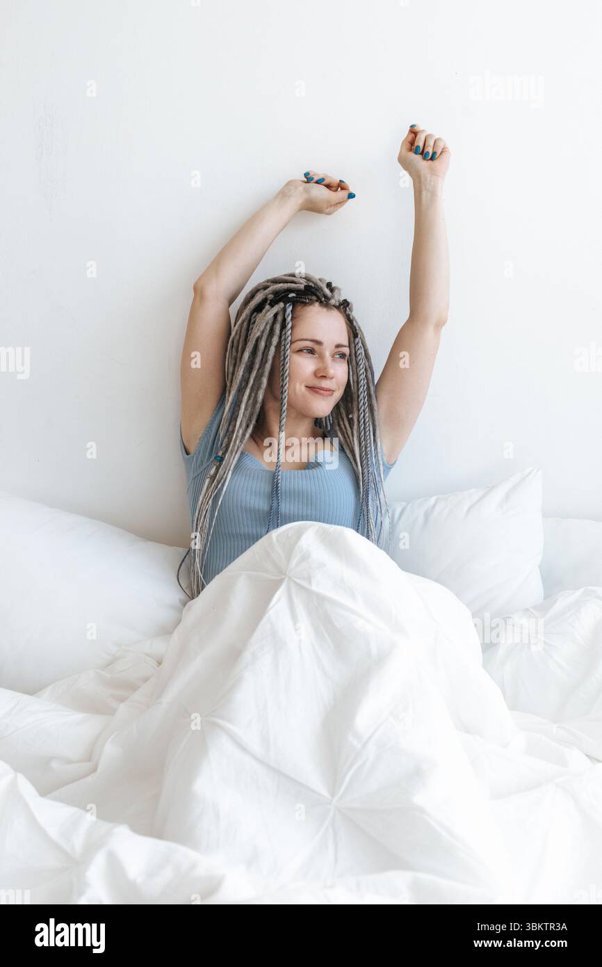 Giovane donna felice che si allunga nel letto bianco. Foto Stock