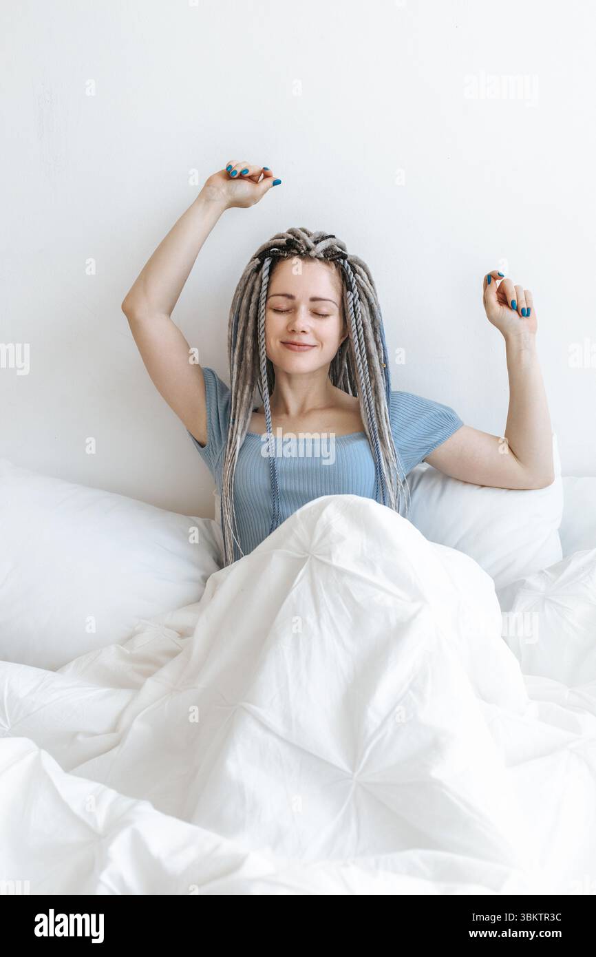 La giovane bella donna felice si sveglia nel letto bianco. Foto Stock
