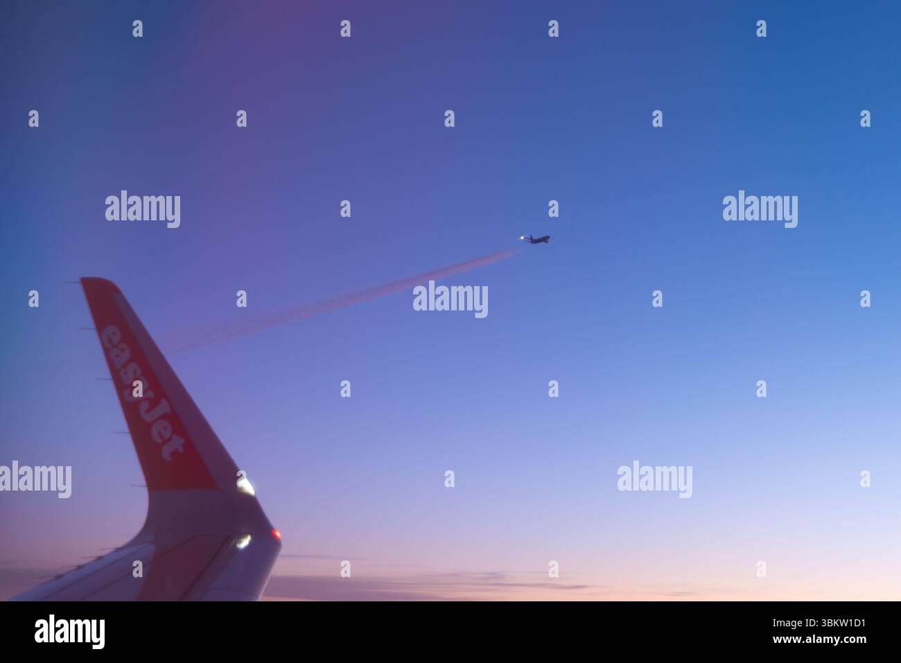 Vista di un tramonto dalla finestra di un aereo Airbus A320 easyJet sopra l'Europa, con una punta alare e un altro aereo di linea su un livello di volo simile Foto Stock