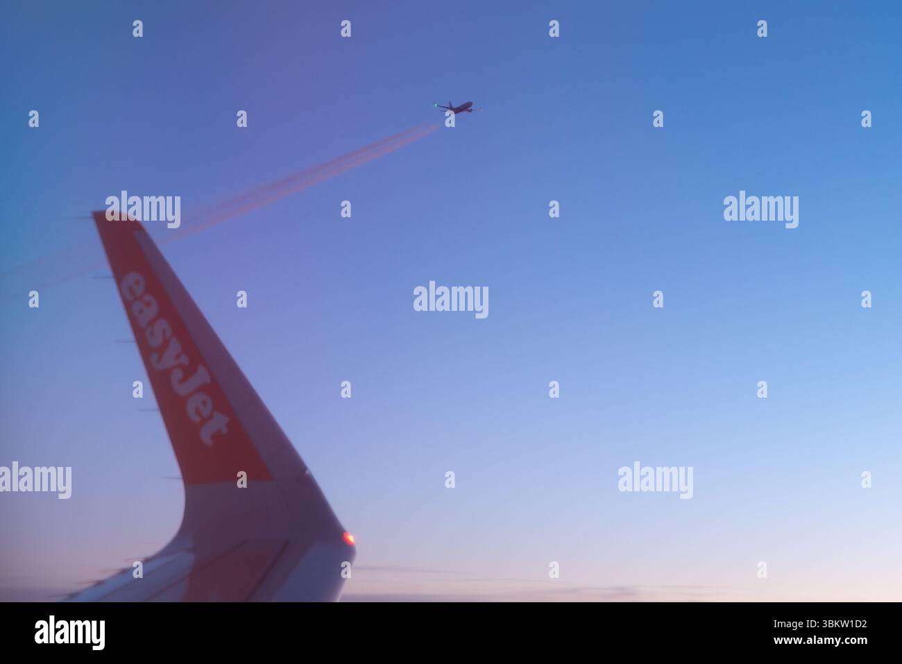 Vista di un tramonto dalla finestra di un aereo Airbus A320 easyJet sopra l'Europa, con una punta alare e un altro aereo di linea su un livello di volo simile Foto Stock