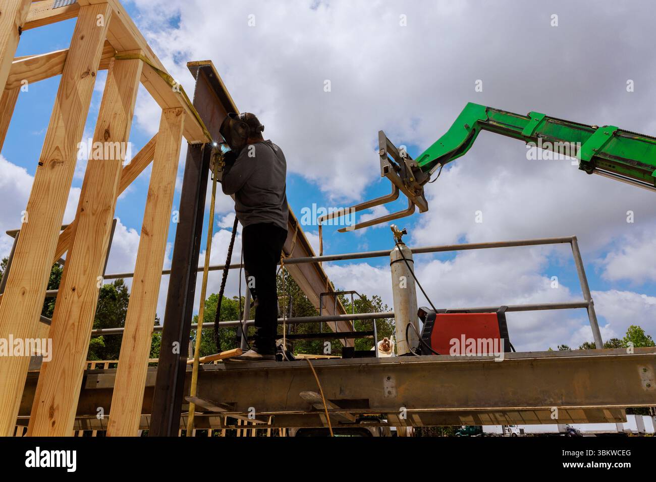 L'operaio edile salda travi in acciaio utilizza la macchina per sollevare le travi strutturali durante il lavoro Foto Stock