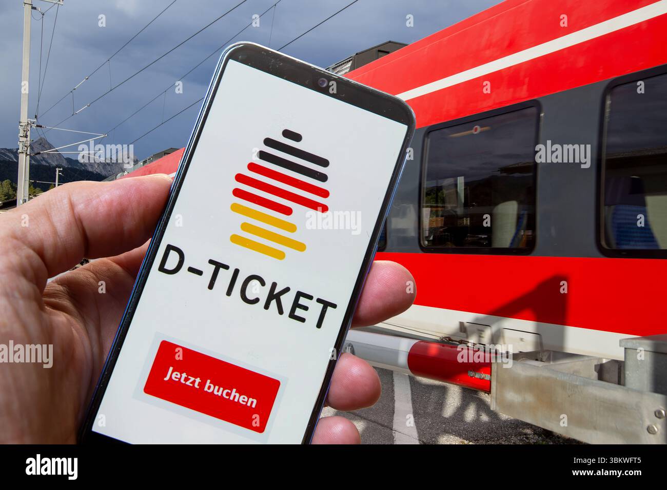 (Fotomontaggio) Logo del Deutschlandticket su uno smartphone di fronte a un treno locale di passaggio Foto Stock