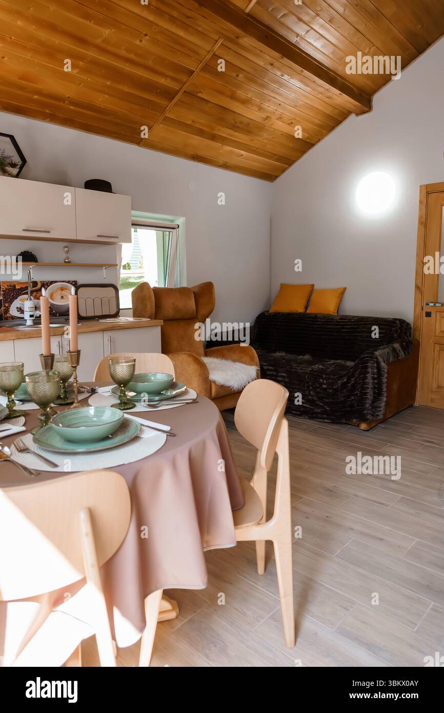 Accogliente ambiente salotto in cabina con tavolo da pranzo per un pasto, comodo divano marrone, calda illuminazione a soffitto e tessuti in legno naturale. p Foto Stock