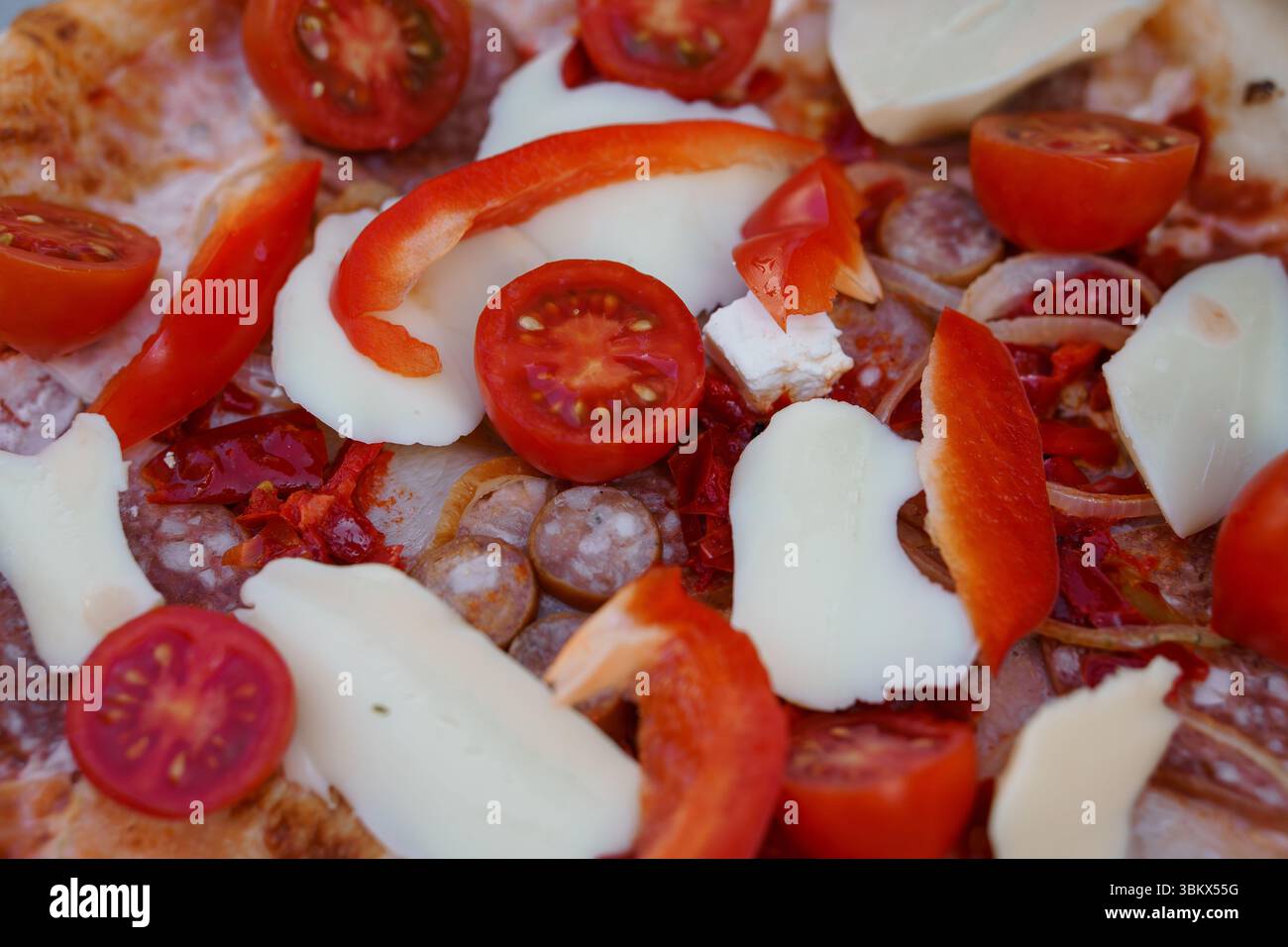 Delizioso primo piano di una pizza italiana appena sfornata condita con pomodori ciliegini maturi, cremose fette di mozzarella, vivaci strisce di pepe rosso e s Foto Stock