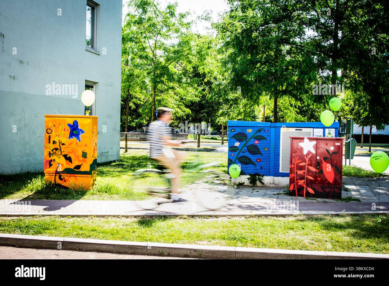 Vivace Street art su scatole multiuso in un ambiente urbano verde con un ciclista in movimento, che cattura l'energia della vita cittadina e degli spazi pubblici creativi. Foto Stock