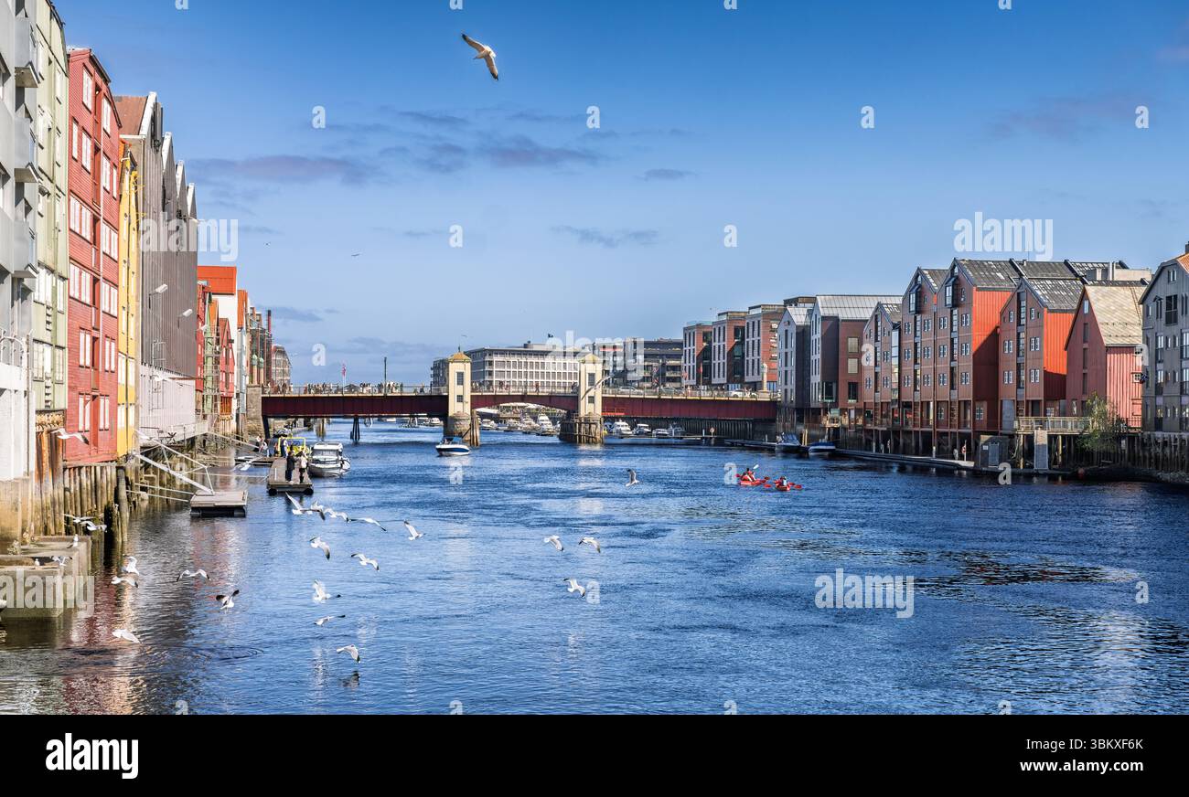 Splendida vista diurna di un tranquillo fiume fiancheggiato da colorati edifici storici sul lungomare sotto un cielo luminoso, con un pittoresco ponte e dist Foto Stock