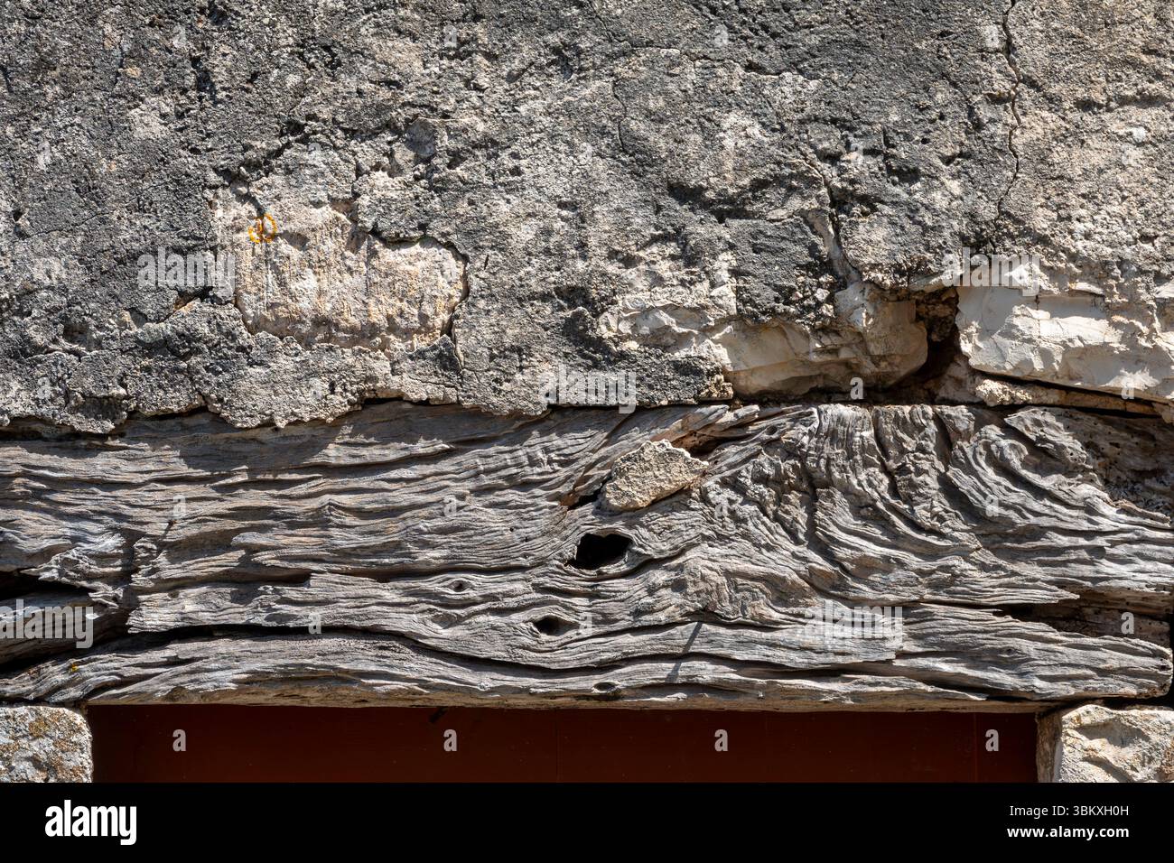 Primo piano di una vecchia trave di legno di quercia che sorregge sopra una parete in pietra e intonaco Foto Stock