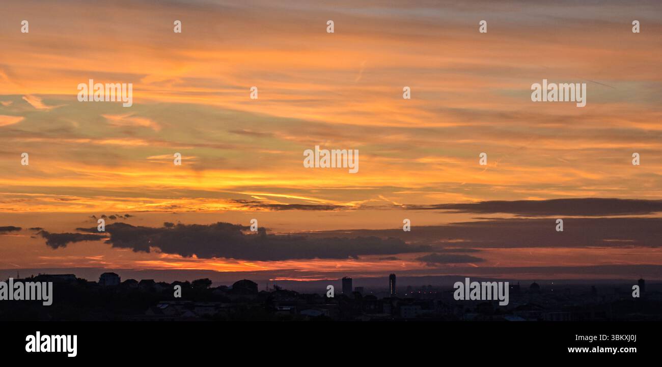 Silhouette dello skyline della città sotto un cielo luminoso al tramonto con nuvole radiose e sfumature morbide di colori caldi Foto Stock