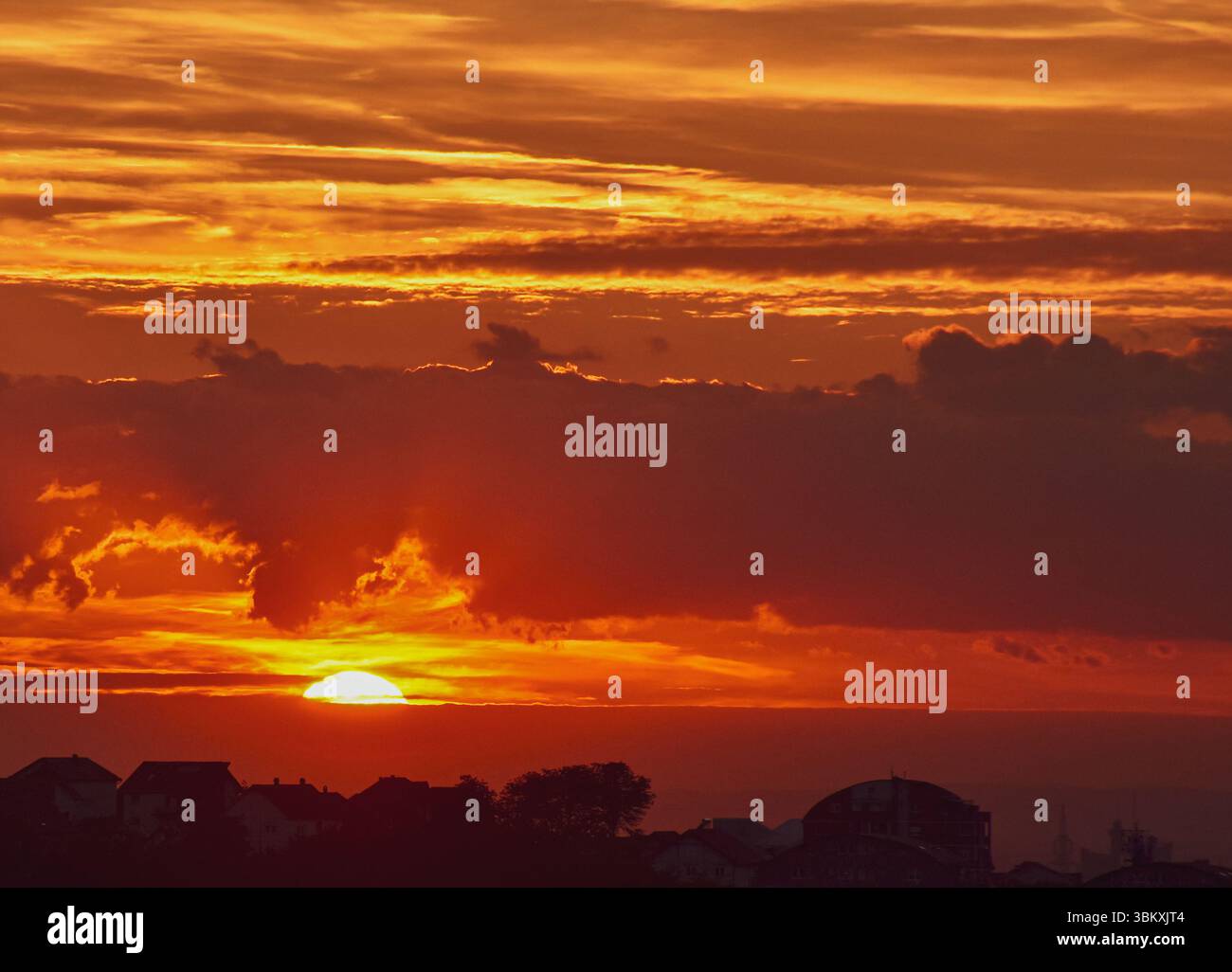 I toni caldi saturi nel cielo sbiadono sulla città buia mentre le nuvole luminose brillano nei raggi finali del sole Foto Stock