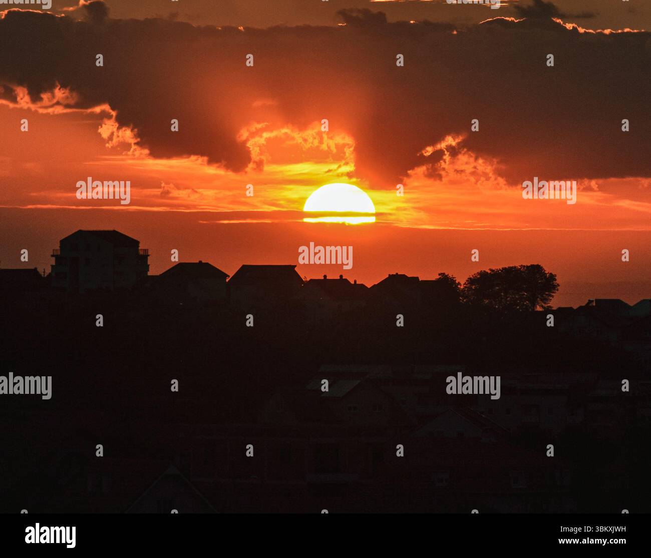 Silhouette urbane sotto un tramonto incandescente, le nuvole a strati riflettono tonalità dorate con accenni di grigio, giallo e arancione ardente. Foto Stock