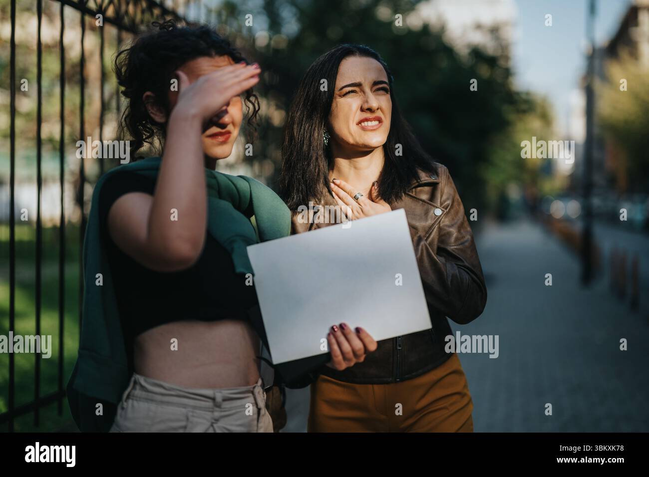 Due donne che proteggono gli occhi dalla luce del sole all'aperto e tengono in mano un documento Foto Stock