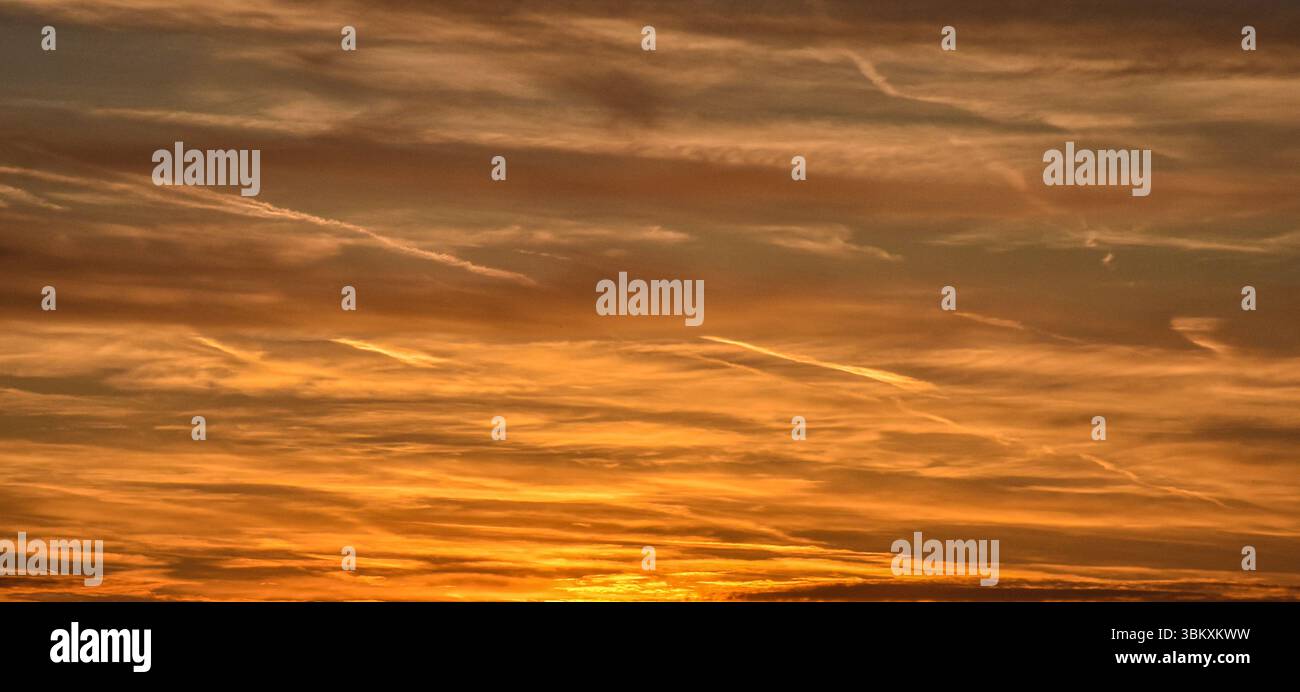 Spettacolare cielo dorato al tramonto con nuvole arancioni brillanti e sfumature di colore tenue che si trasformano in tonalità blu e grigio caldo Foto Stock