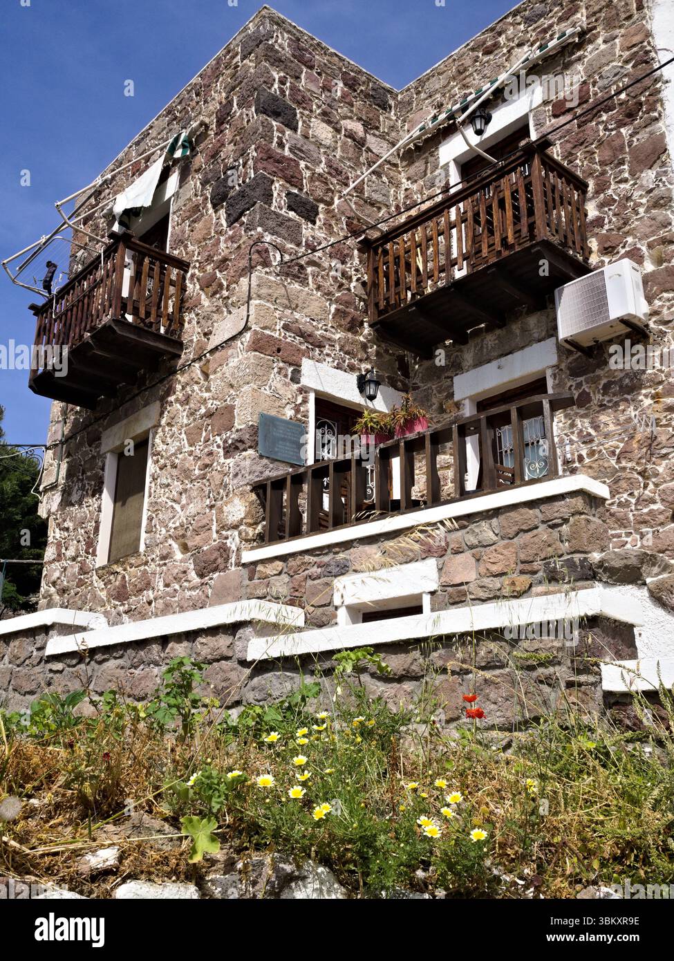 Facciata rustica di case mediterranee con pareti in pietra, balconi in legno e erba secca sottostante, evocando il fascino rurale estivo. Foto Stock