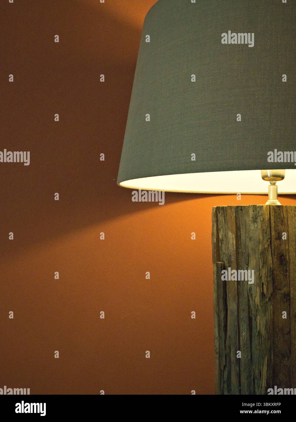Lampada da lettura rustica con base in legno e piano in tessuto illuminata con calore contro pareti di rosso scuro, atmosfera accogliente ed elegante. Foto Stock