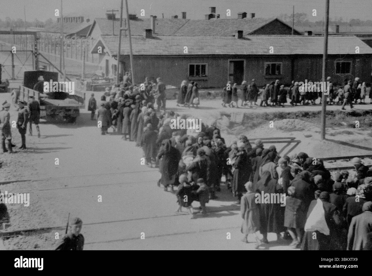 AUSCHWITZ, POLONIA - maggio 1944 - donne e bambini ebrei che sono stati selezionati per la morte, camminano in fila verso le camere a gas. Il cancello in alto Foto Stock