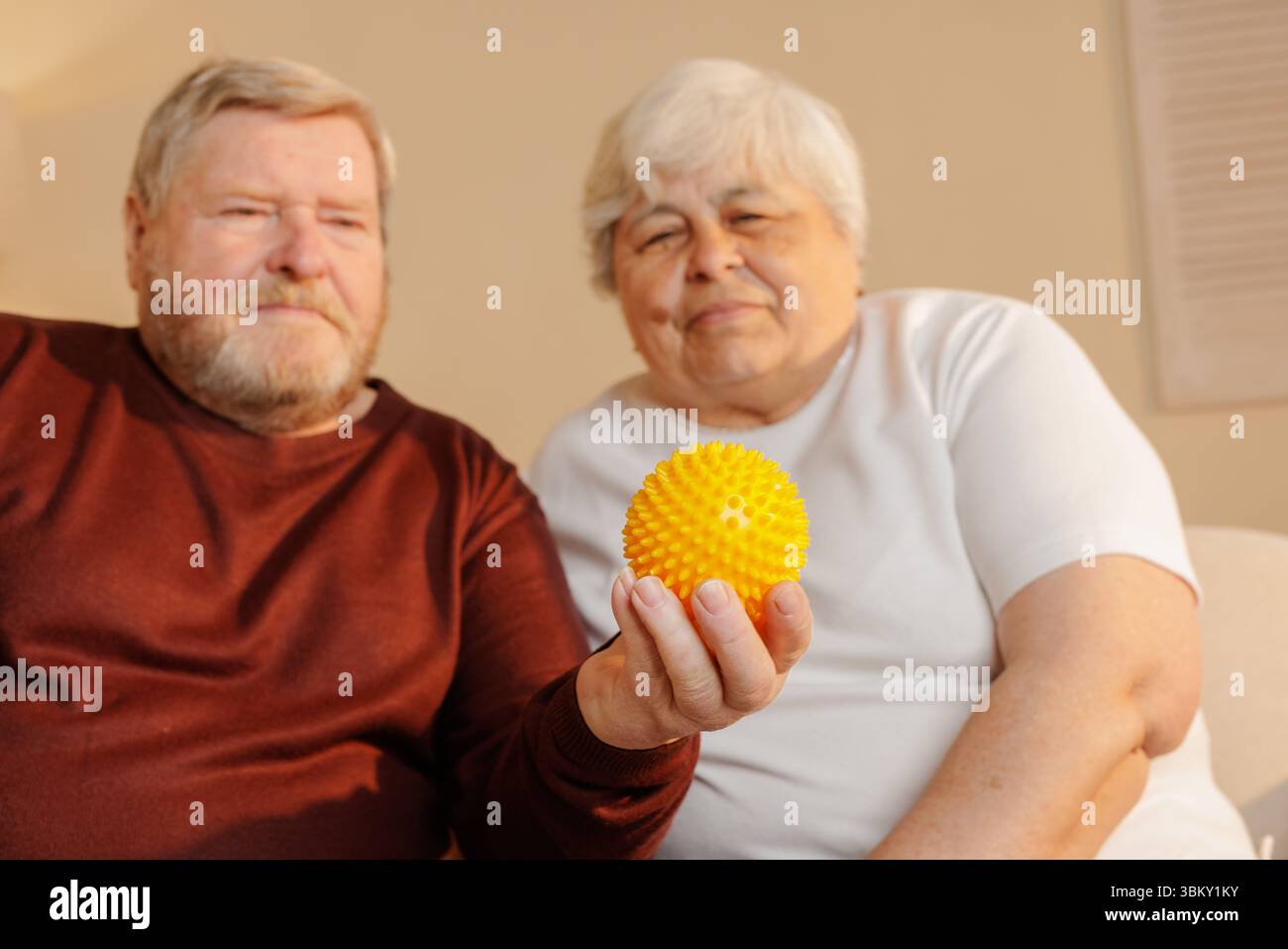 Coppia anziana con una palla di massaggio giallo per alleviare il dolore riabilitando e supportando il benessere a casa Foto Stock