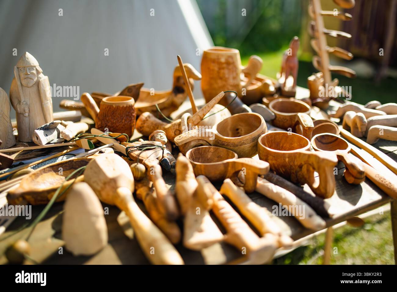 Una varietà di utensili in legno intagliati a mano, figure e strumenti sono esposti su una tavola in un festival archeologico medievale, che riflette il tradizionale c Foto Stock