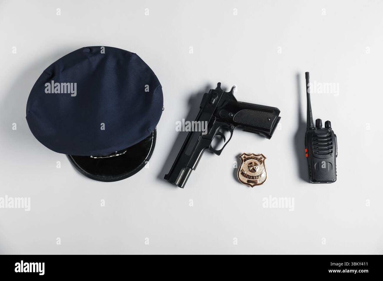 Cappellino della polizia, pistola, distintivo e walkie talkie su sfondo bianco, piatto Foto Stock