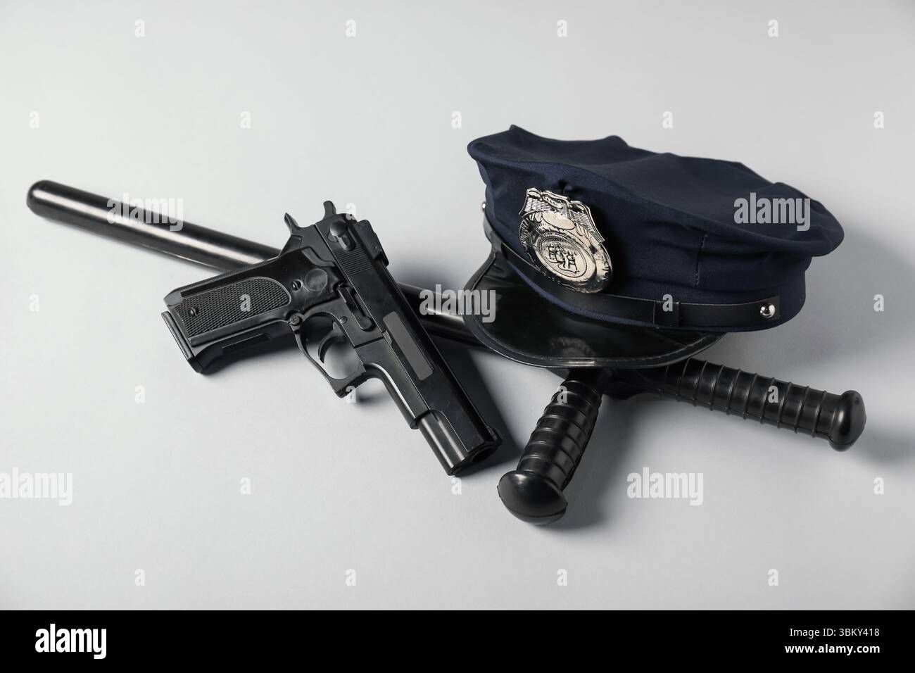 Cappello della polizia, pistola e bastone su sfondo bianco Foto Stock