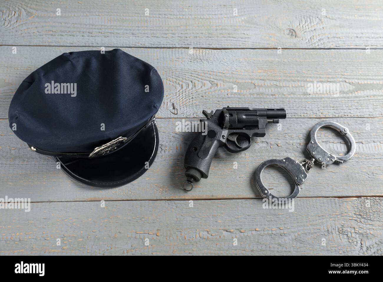 Cappellino, pistola e polsini da polizia su tavolo in legno grigio, piatto Foto Stock