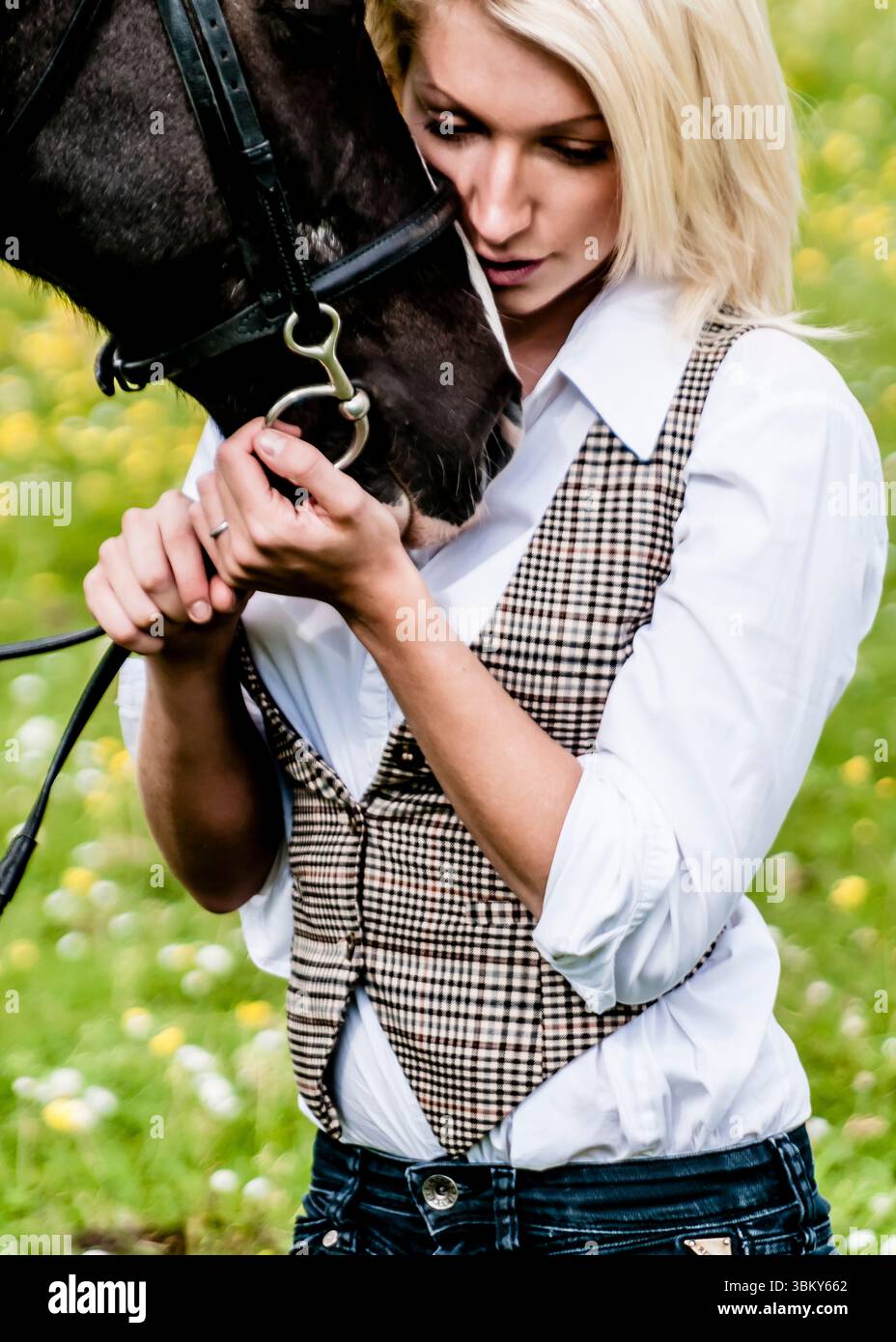 Una donna con una camicia bianca e un gilet a quadri abbraccia un cavallo nero, che ne tiene le briglie. Foto Stock